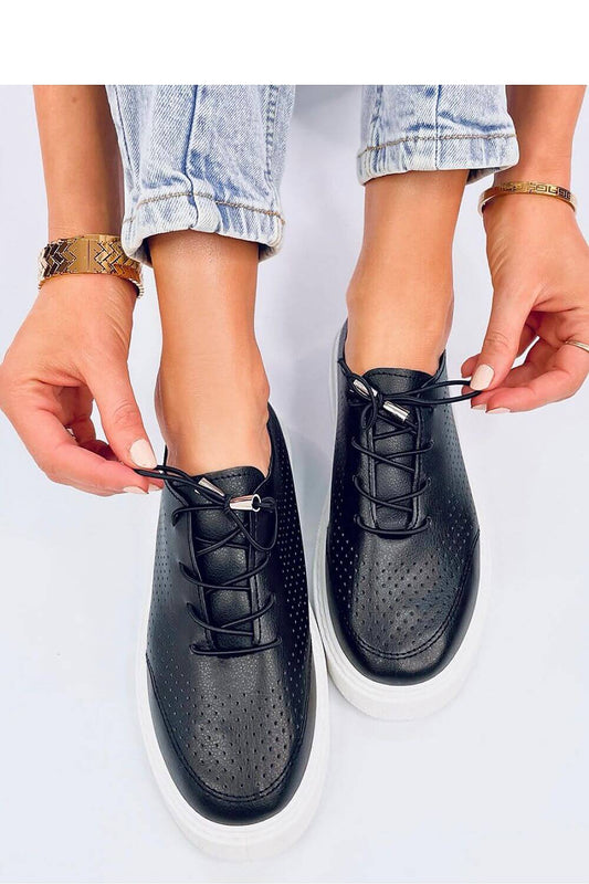 Woman tying laces on black perforated eco-leather sneakers with high sole, showcasing stylish and comfortable Inello model 192589.