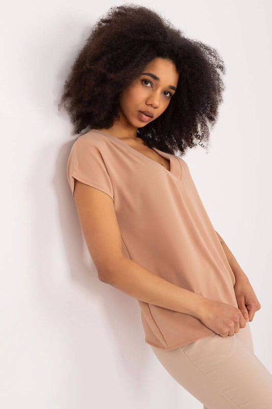 Woman in casual V-neck beige blouse, standing against white wall, showcasing everyday style and comfort.