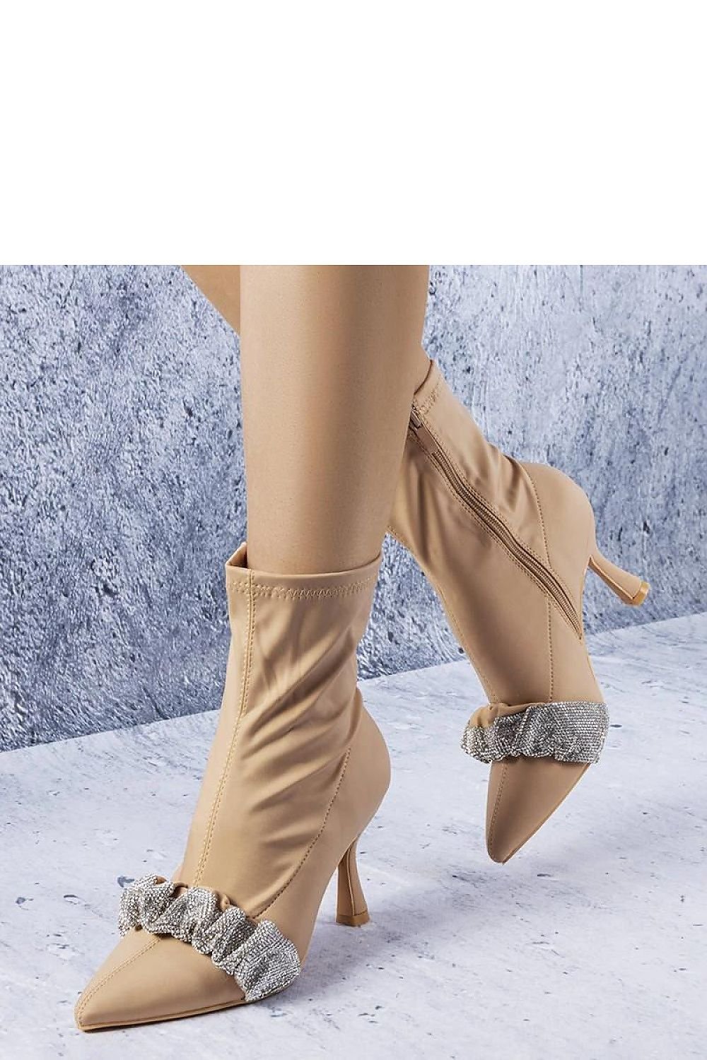 Elegant tan stiletto ankle boots with ruffle detail and side zipper on a textured background.