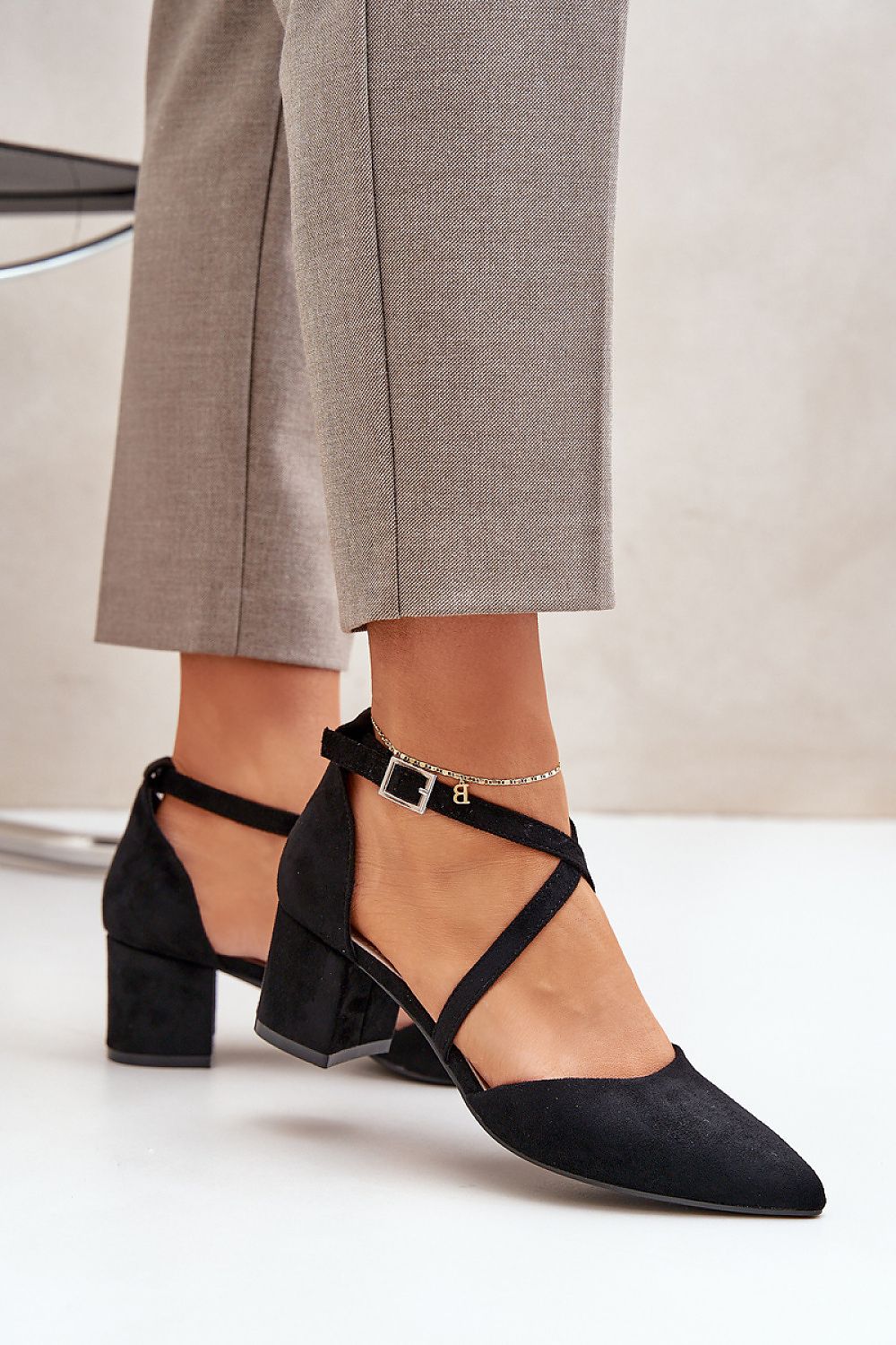 Elegant black heeled shoes with criss-cross straps and ankle buckle, paired with gray pants.