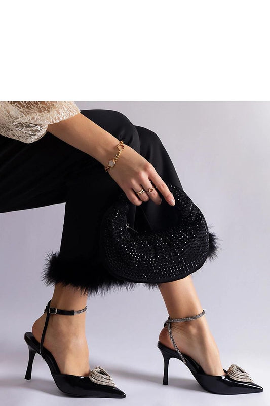 Elegant woman wearing black open-back stilettos with rhinestone accents, featuring a matching sparkling clutch and stylish black pants.