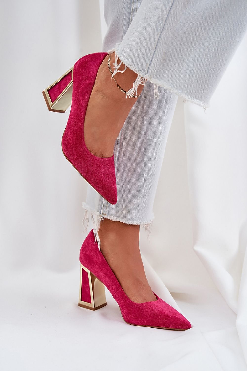 Pink high-heeled suede pumps with elegant pointed toes and mirrored heels, paired with frayed jeans for a chic look.