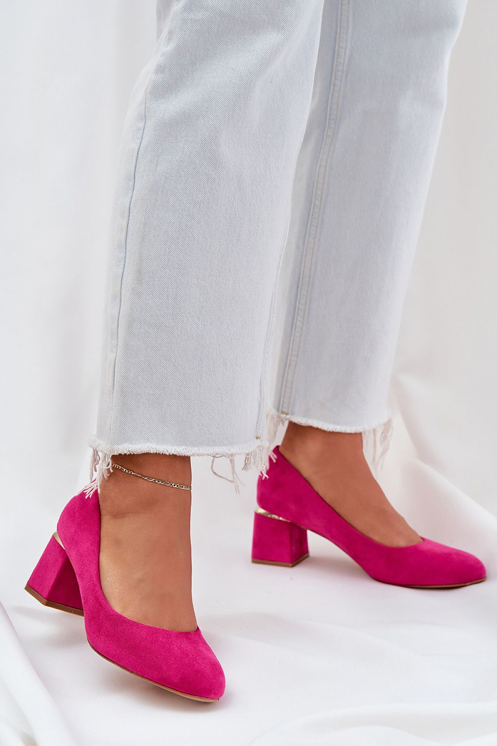 Hot pink high-heeled court shoes paired with frayed light jeans, featuring subtle gold heel detail for chic elegance.