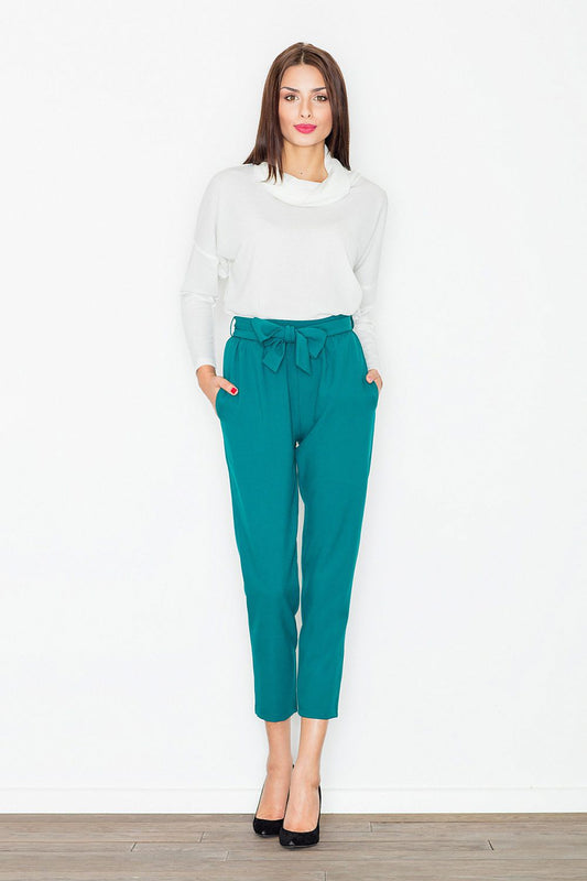 Woman wearing teal trousers with decorative waist tie and pockets, Figl Model 77114, full length view against a white background.