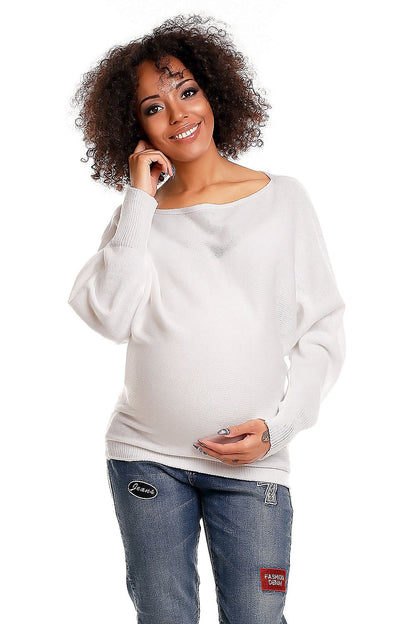 Smiling woman in white oversized maternity sweater with kimono style sleeves and boat neckline, pairing with jeans.