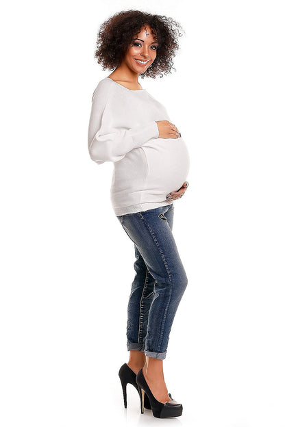 Pregnant woman wearing an oversized maternity sweater with boat neckline and kimon style, paired with jeans, smiling joyfully.