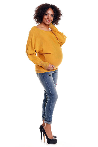 Woman wearing an oversized mustard maternity sweater and jeans, showcasing fashion-forward style and comfort for expectant mothers.