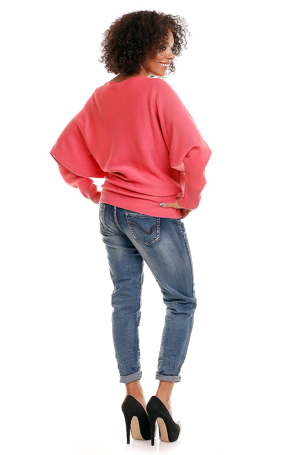 Woman in pink oversized maternity pullover model 84269 PeeKaBoo with kimono sleeves and boat neckline, paired with jeans and heels.