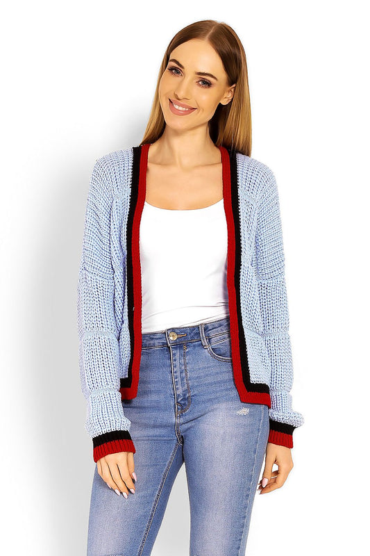 Model wearing blue knitted cardigan with contrasting black and red trim, styled open over white top and jeans. Stylish loose-fit look.