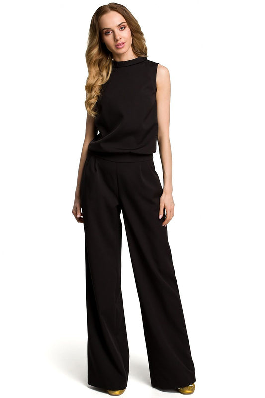 Chic woman in black jumpsuit combining elegance and casual comfort, showcasing Moe's Overál model 117565 with open back and sleek design.