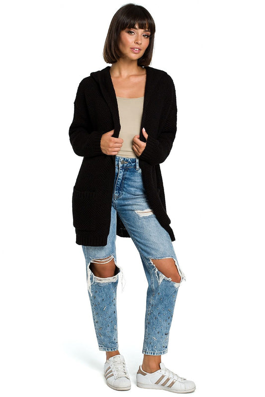 Woman wearing Kardigán model 121225 BE Knit long black cardigan with hood, ribbed cuffs, and pockets, styled with ripped jeans.