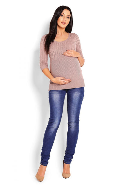 Pregnant woman wearing a fine knit maternity pullover with cables, 3/4 sleeves, and a round neck in beige, paired with blue jeans.