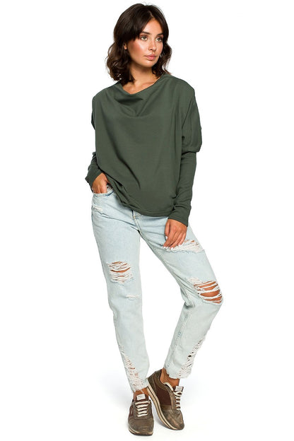 Woman modeling a casual green pullover with a draped neckline and ribbed sleeves, paired with ripped jeans.