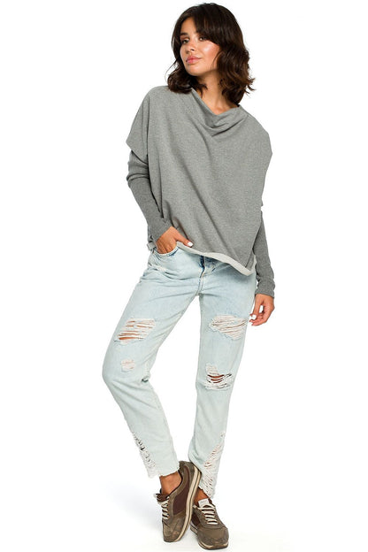 Woman in casual grey BeWear pullover with draped neckline and ribbed sleeves, paired with ripped jeans for a trendy look.