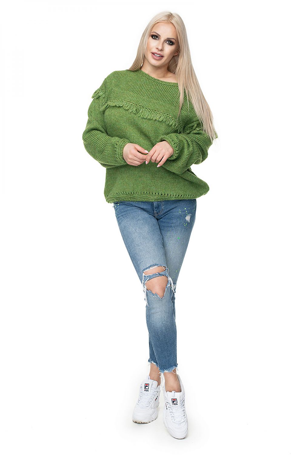 Woman wearing green Pulóver model 131603 by PeeKaBoo, featuring decorative front tassels, paired with ripped jeans and white sneakers.