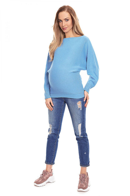 Model wearing blue oversized maternity pullover with kimono cut and boat neckline, paired with ripped jeans and sneakers.