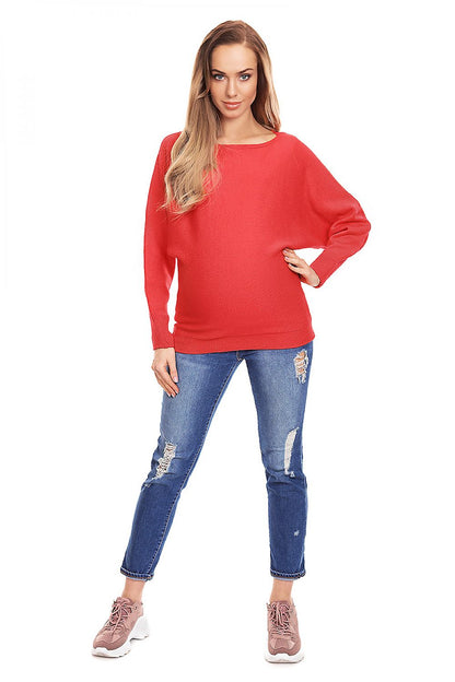 Pregnant woman wearing red oversized maternity sweater with ripped jeans and sneakers, showcasing boat neckline and kimono sleeves.