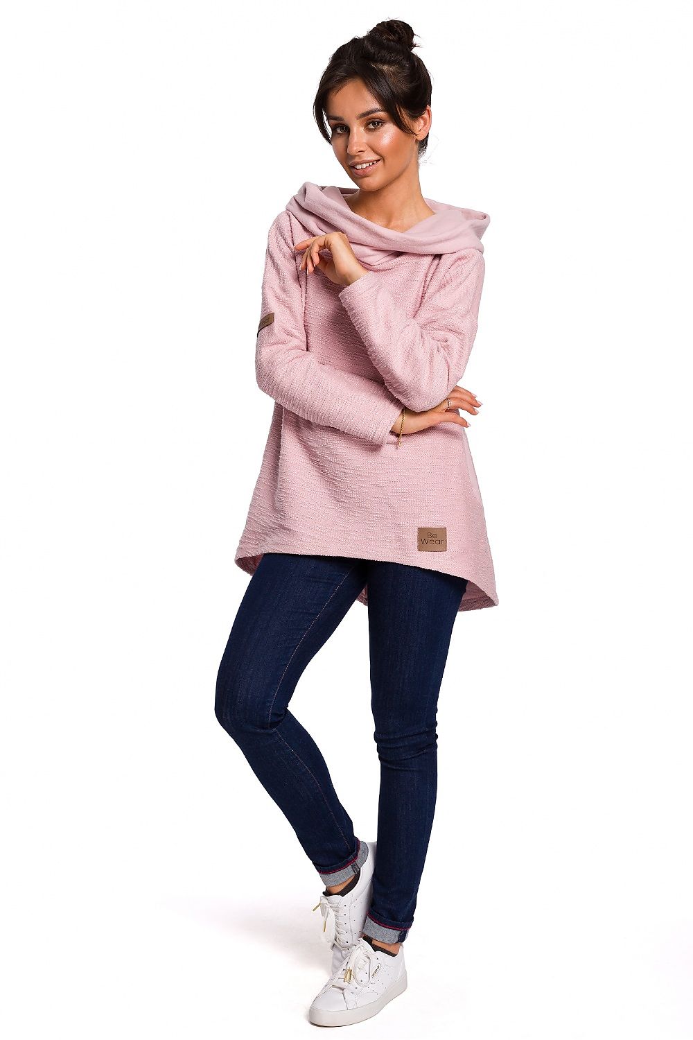 Woman wearing pink asymmetrical BeWear pullover with pockets, styled in casual jeans and sneakers, ideal for chilly weather.