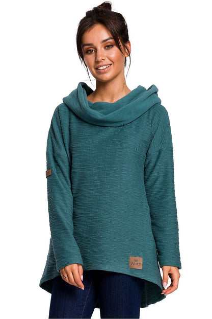 Woman wearing teal asymmetric pullover with cowl neck and hood, perfect for colder seasons. BeWear Model 134537.