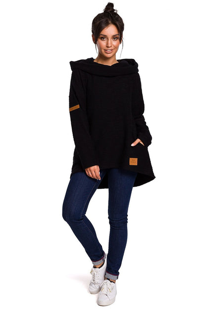 Woman wearing black asymmetrical hoodie with pockets and hood, standing confidently. Perfect for colder seasons. Stylish comfort.