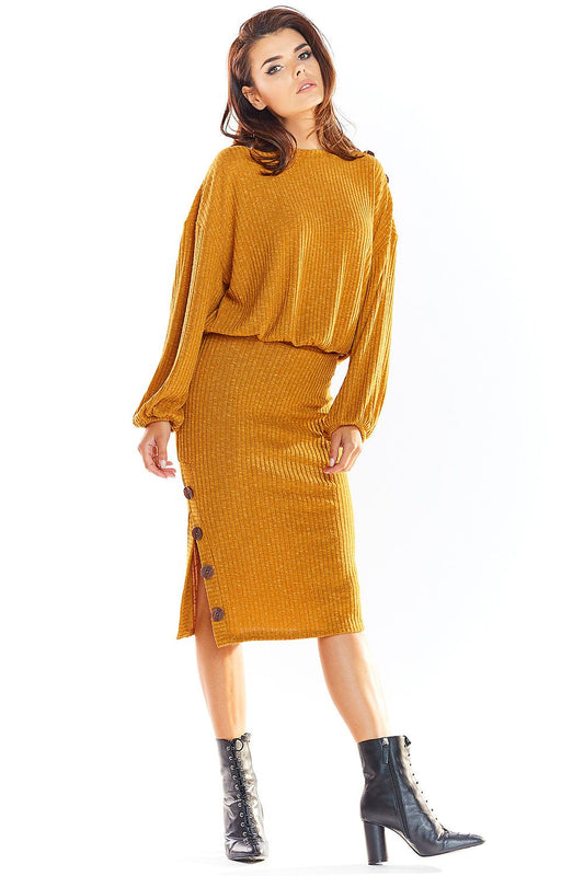 Model wearing mustard oversized pullover with button details and matching skirt, styled with black ankle boots.