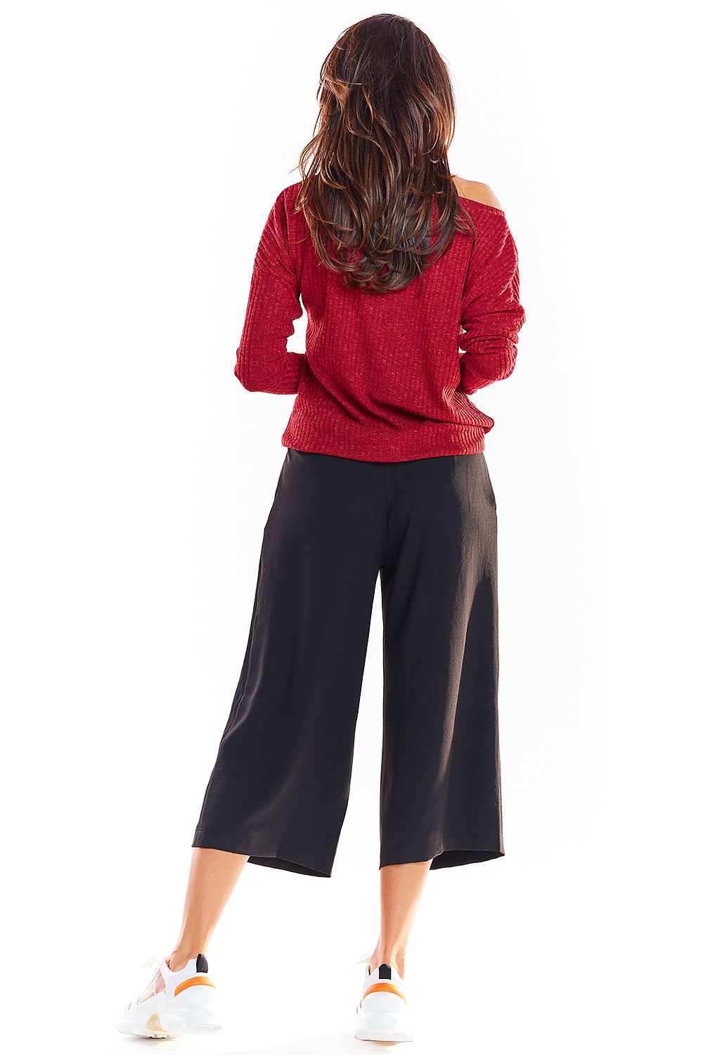 Woman wearing red pullover with black culottes, back view.