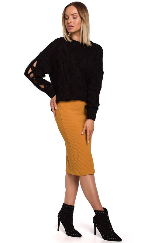 Stylish woman in Pulóver Model 147412 Moe, featuring unique cracked sleeves and chic cable design, paired with a mustard pencil skirt and ankle boots.