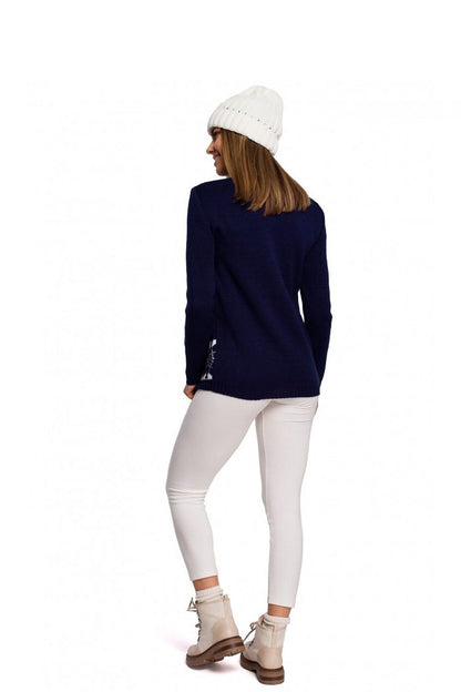 Woman wearing navy blue Christmas pullover with reindeer motif, paired with white pants, beige boots, and a white beanie, back view.