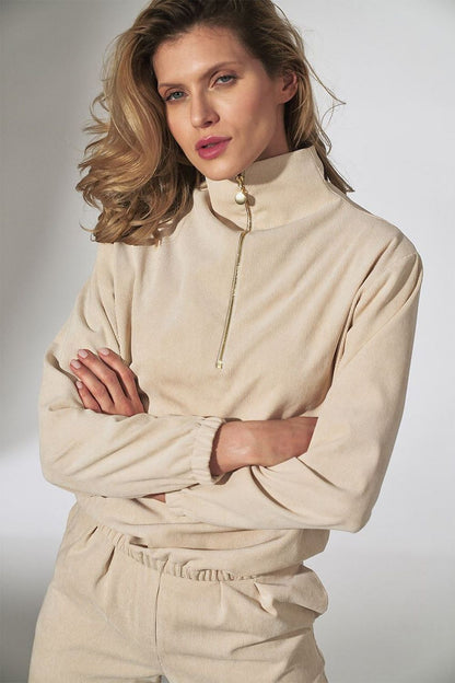 Stylish woman wearing a beige collared pullover with zip detail and elastic cuffs, exuding casual elegance.