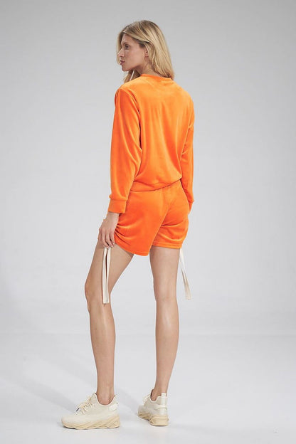 Woman wearing orange velour leisure set with ribbed cuffs, featuring Szabadidőfelső model 154668 by Figl. Side view.