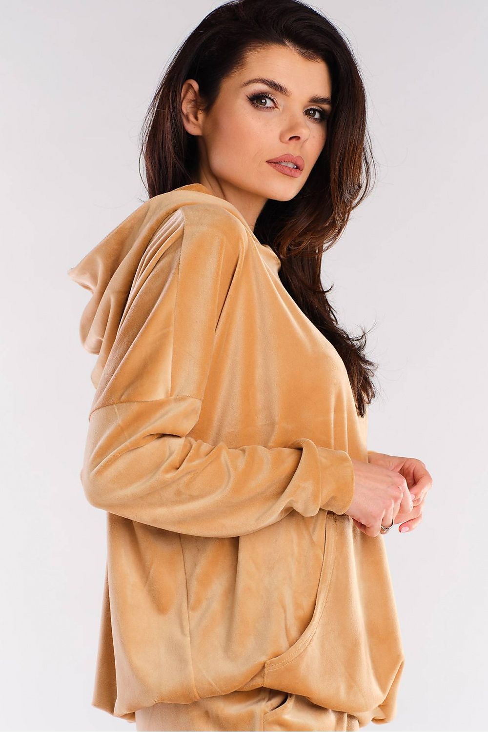 Woman wearing a stylish tan velour hoodie with a large pocket and hood, embodying trendy urban fashion.