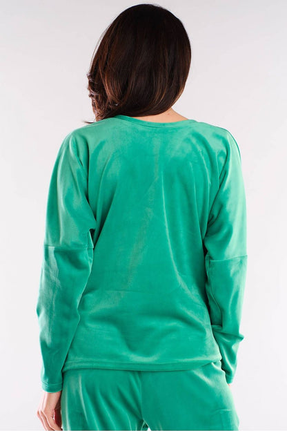 Model wearing green sweatshirt with relaxed fit and V-neck, showing back view in stylish urban fashion.