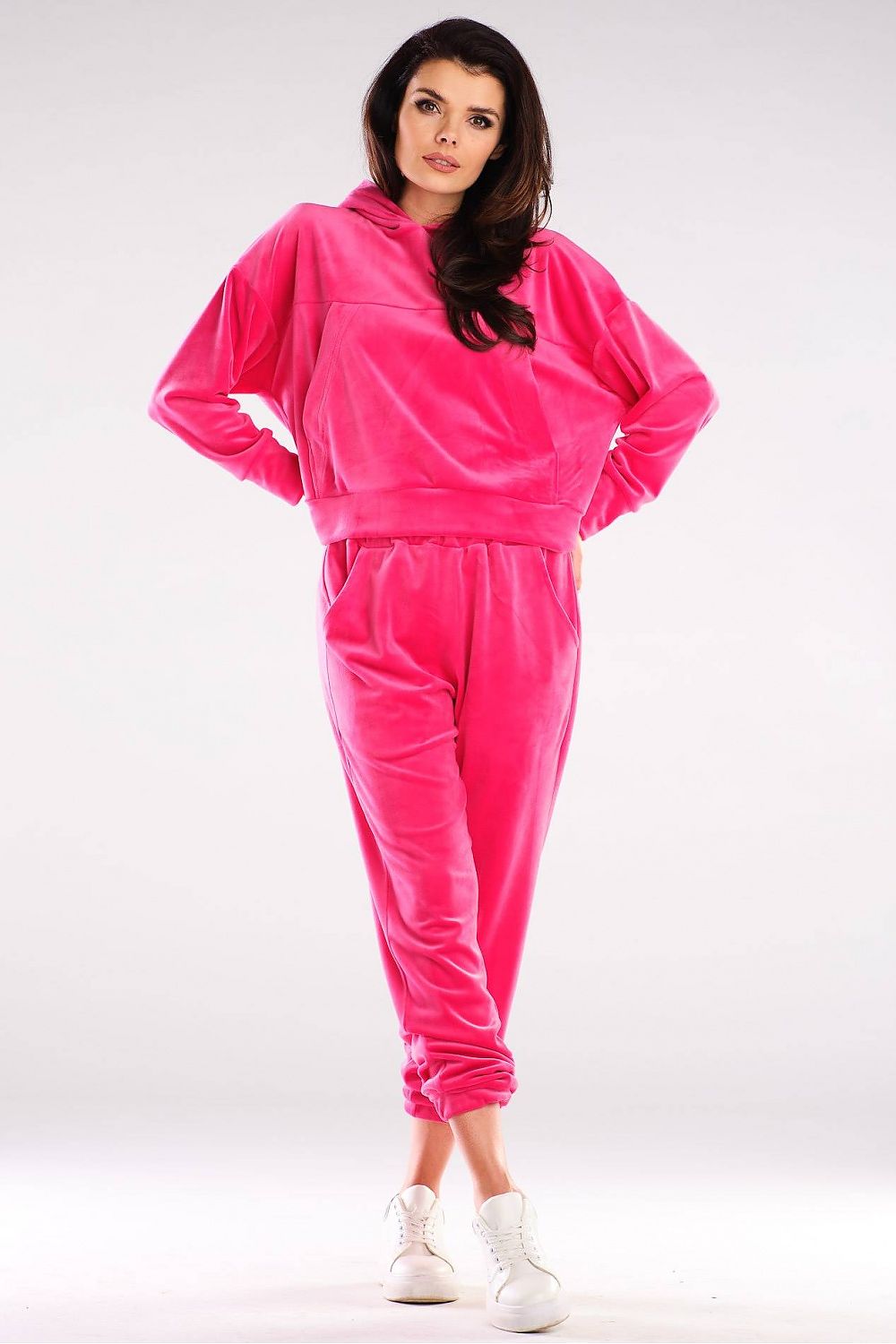 Woman wearing a vibrant pink velour hoodie and joggers set, showcasing comfortable loungewear paired with white sneakers.