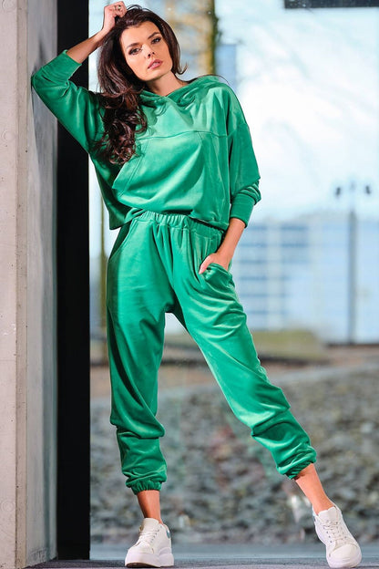 Woman wearing green velour hooded kangaroo pocket pullover and joggers, designed and made in Poland. Stylish casual outfit.