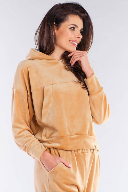 Woman wearing a cozy velour hooded kangaroo pocket sweatshirt in camel color by Awama, perfect with jeans or sneakers.