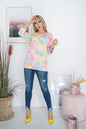 Woman in colorful tie-dye top and jeans standing in stylish room with plants and art.