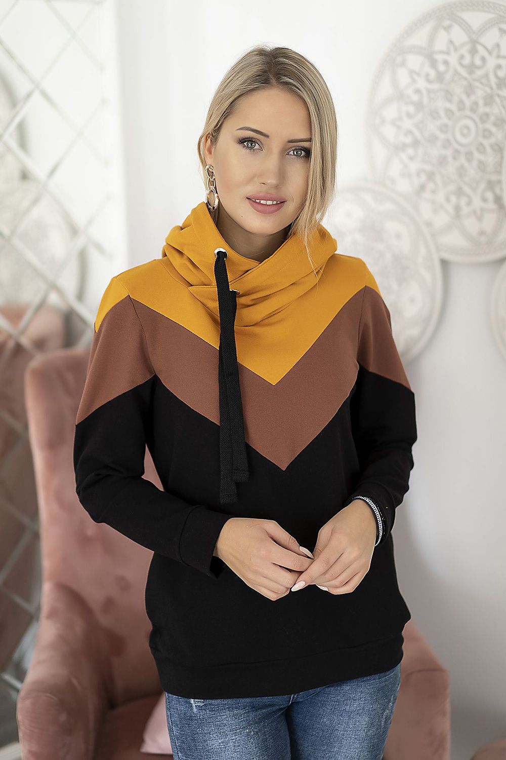 Trendy tri-color hooded pullover, orange-brown-black design, worn by model standing in stylish indoor setting.