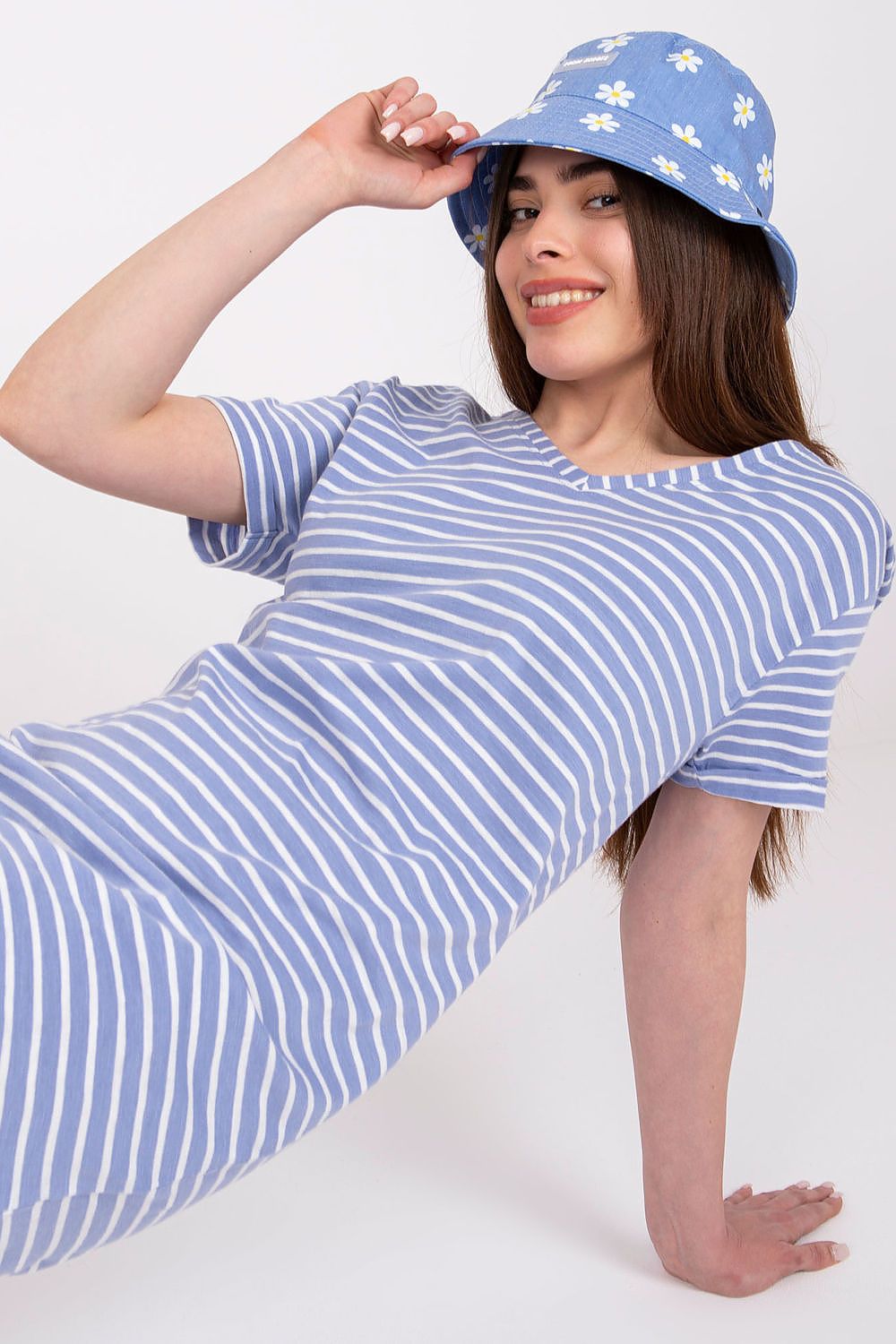 Woman wearing blue striped summer dress and daisy bucket hat, leaning back and smiling.