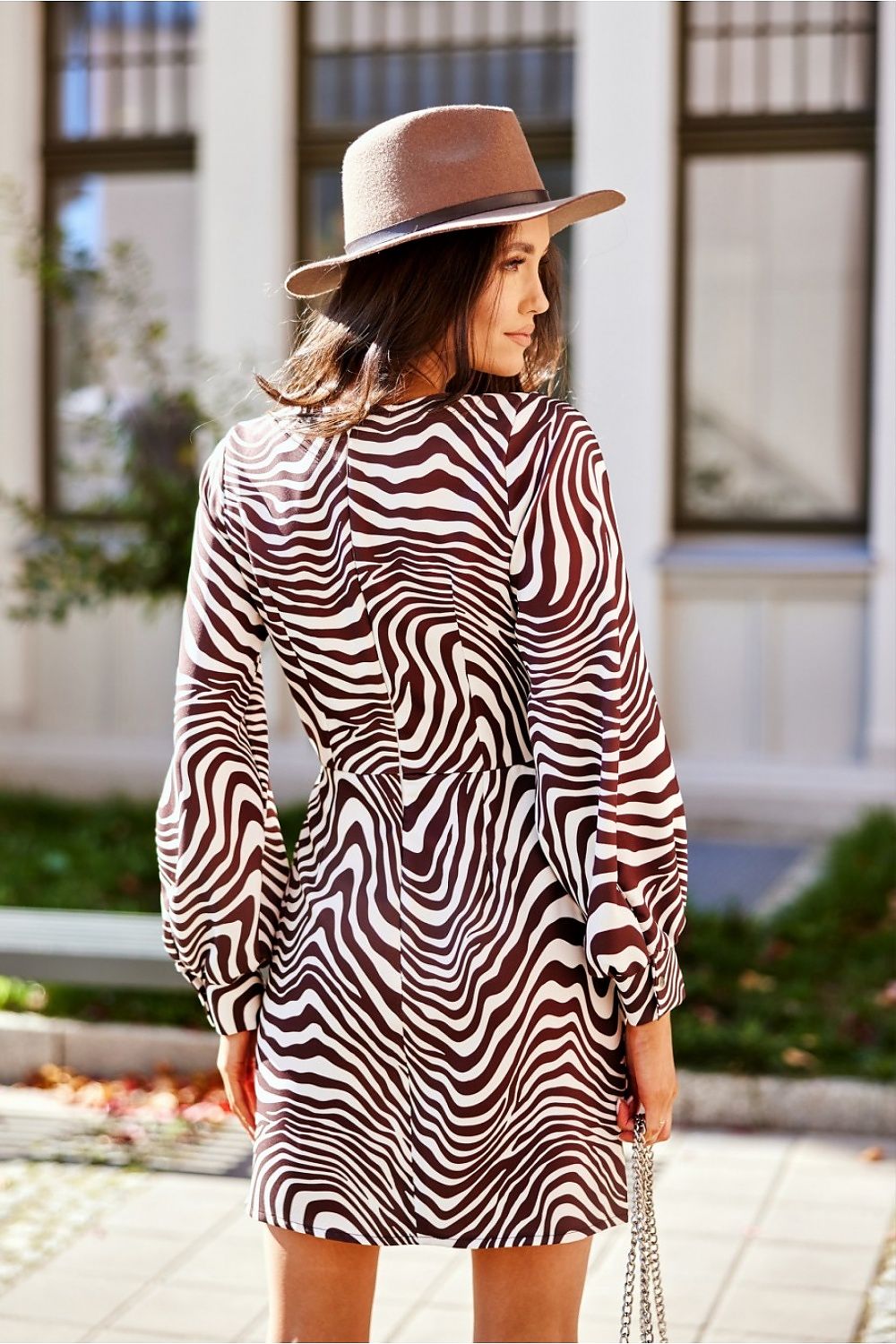 Woman wearing zebra-print dress with balloon sleeves and a hat, standing outside.