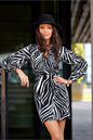 Woman wearing black and white zebra print mini dress with deep neckline and long puff sleeves, styled with a black hat.