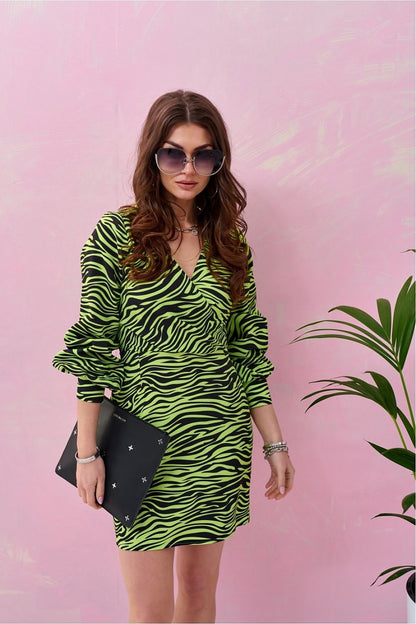 Woman wearing zebra print mini dress with deep neckline and puff sleeves, holding clutch, against pink background with green plant.