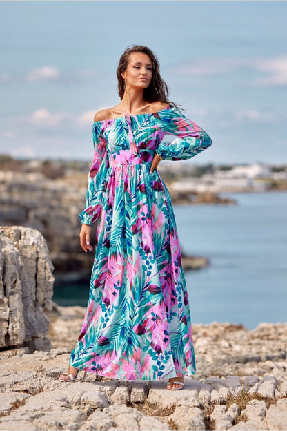 Woman wearing colorful off-shoulder maxi dress by the ocean, showcasing vibrant tropical design from Roco Fashion's latest collection.