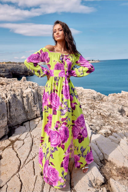 Woman wearing a vibrant floral off-shoulder maxi dress by the sea.