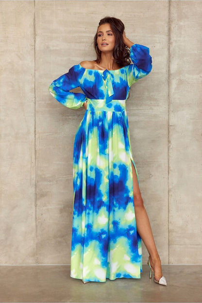 Model wearing a Roco Fashion Spanish-style maxi dress with tie neckline and side slit, featuring vibrant blue and green patterns.